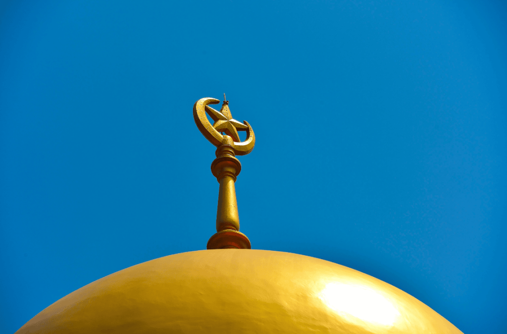 Perspective view of golden dome of a mosque with crescent and star set against a clear blue sky as background with space for copy