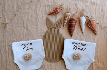 Two baby diapers with bunny tail and carrot garland for twin pregnancy announcement.