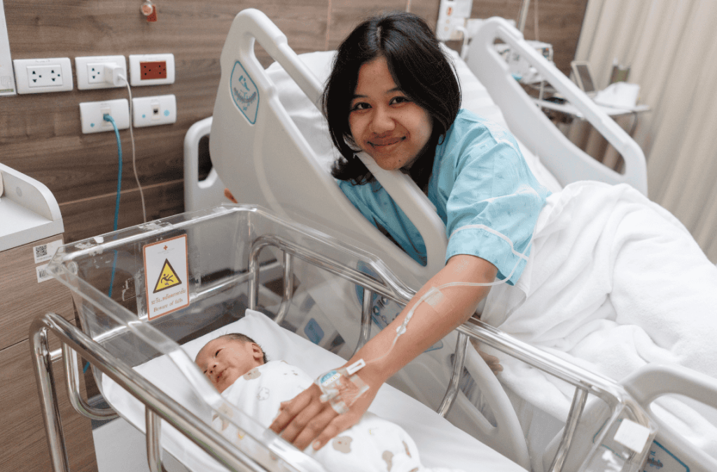 Happy Asian mother looking at her newborn baby in a hospital bassinet.