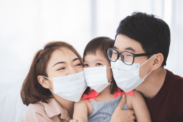 Asia Family in medical masks on the face looks at the camera while standing in the living room at home